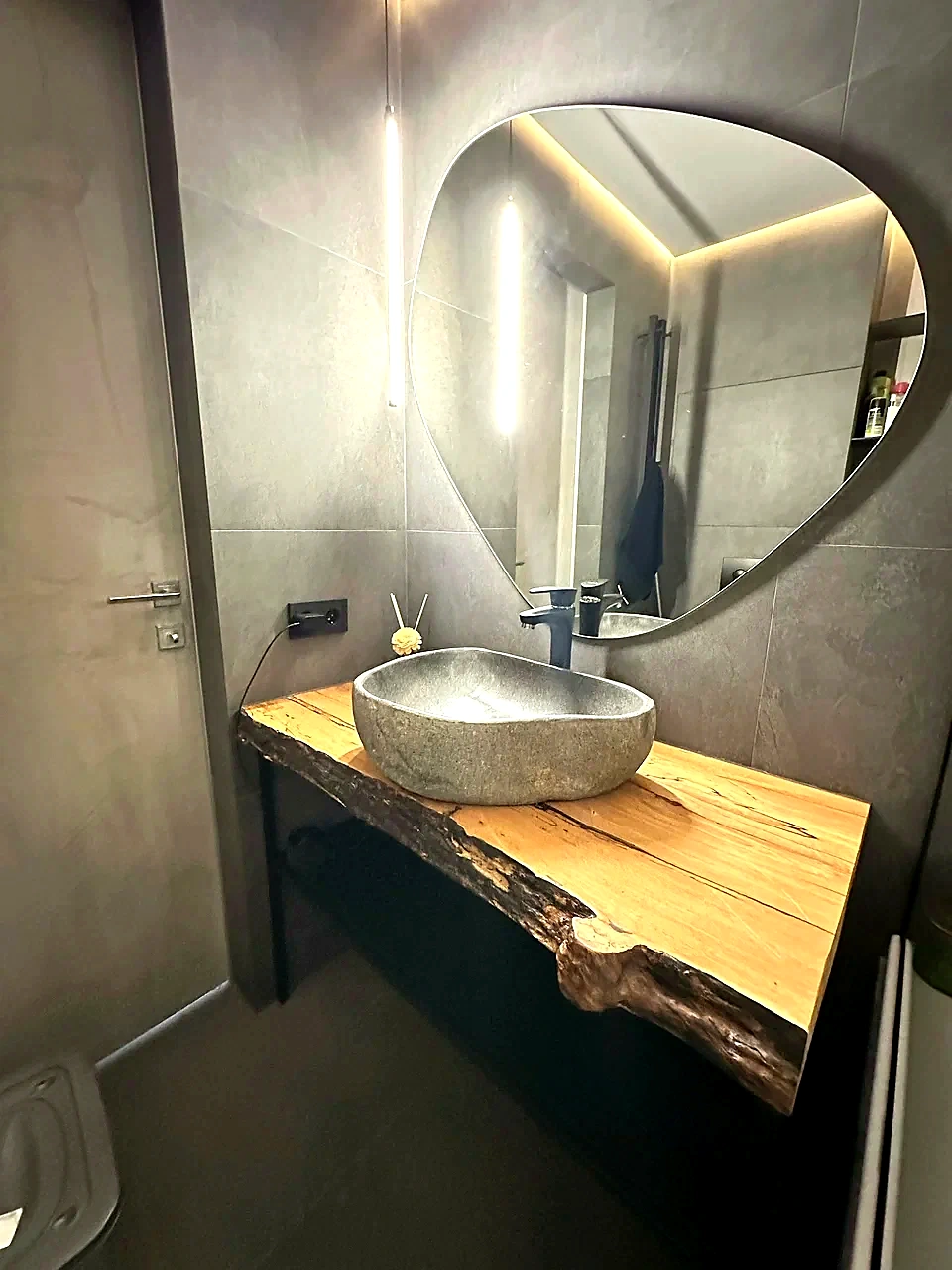 Natural river stone vessel sink on a live edge wood vanity in a modern bathroom with an illuminated mirror