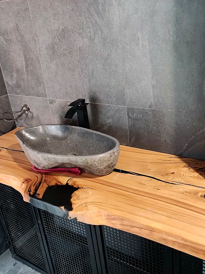 River stone vessel sink installed on a wooden bathroom cabinet with a black faucet